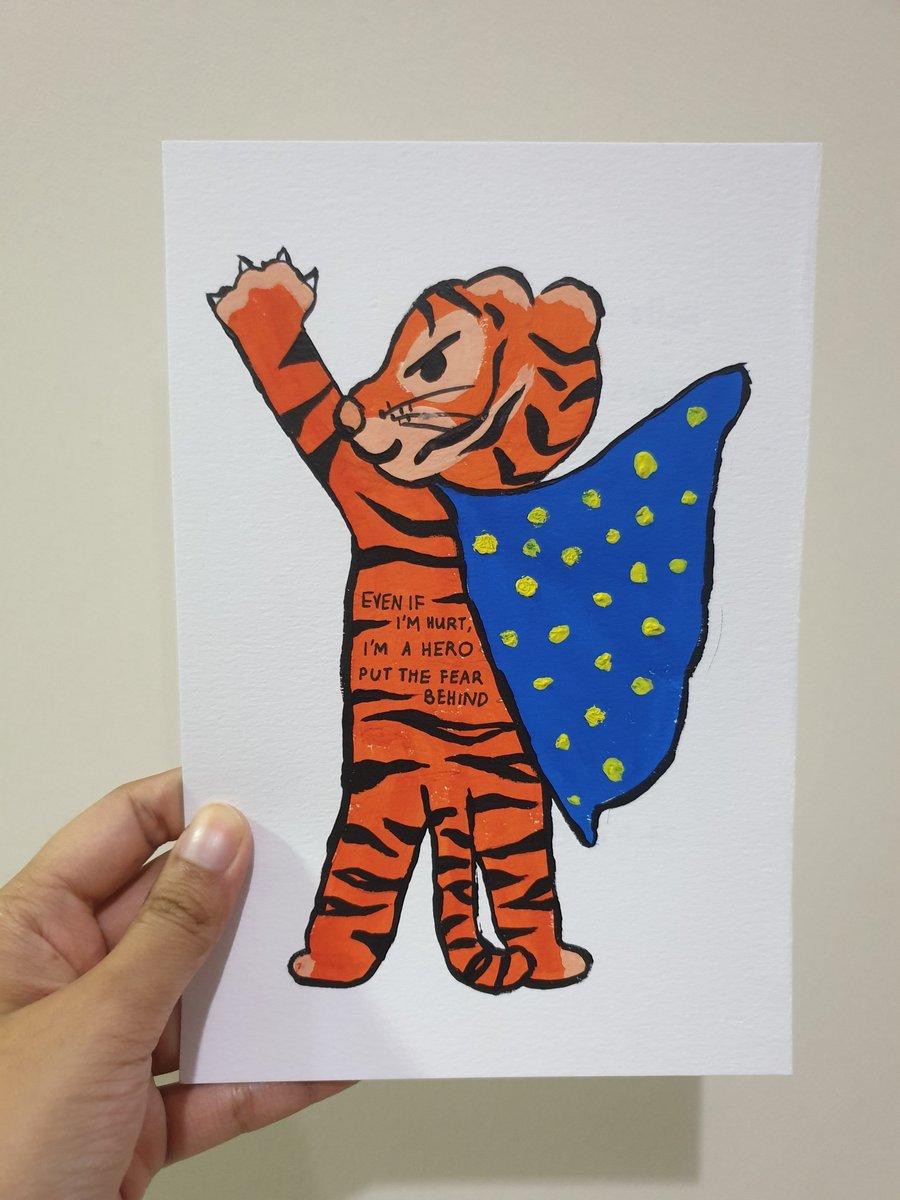 Photo of a hand painted card. The card is of a tiger standing on its hind legs, looking over it's shoulder, with one paw raised which mimics a part of the choreography from BTS' song Anpanman. Written on the tiger's body is a lyric from Anpanman which says "even if I'm hurt, I'm a hero. Put the fear behind"