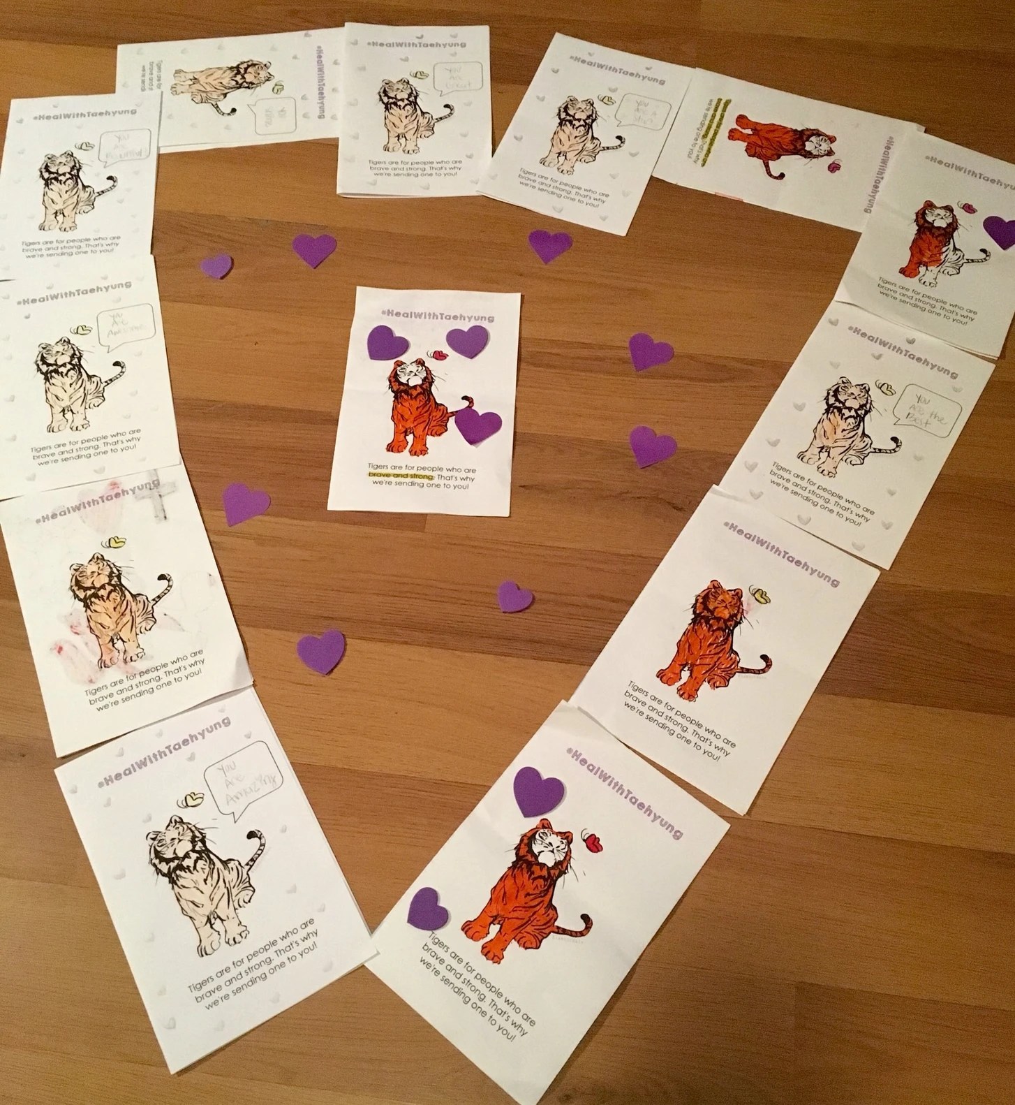 Photo showing printed out colouring pages of tigers. They've ben arranged on the floor in the shape of a heart. Purple hearts cut out of construction paper are scattered inside the heart outline.