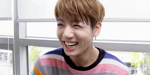 Gif of Jungkook with an open mouthed smile. His hair is styled in a choppy bowl cut. It is light brown with blond highlights. His shirt is striped in multiple colours.