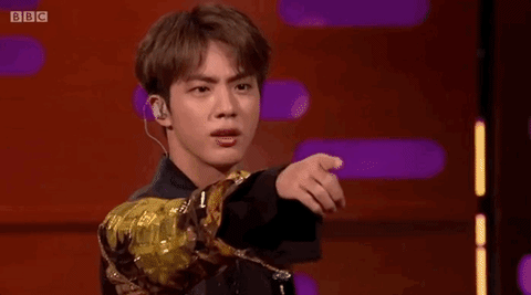 Gif of Seokjin pointing at the camera and blowing a hand kiss. His hair is a medium brown bowl cut with a part in the middle of his bangs. He's only visible from the shoulders up, but he's wearing a black and gold modern hanbok.