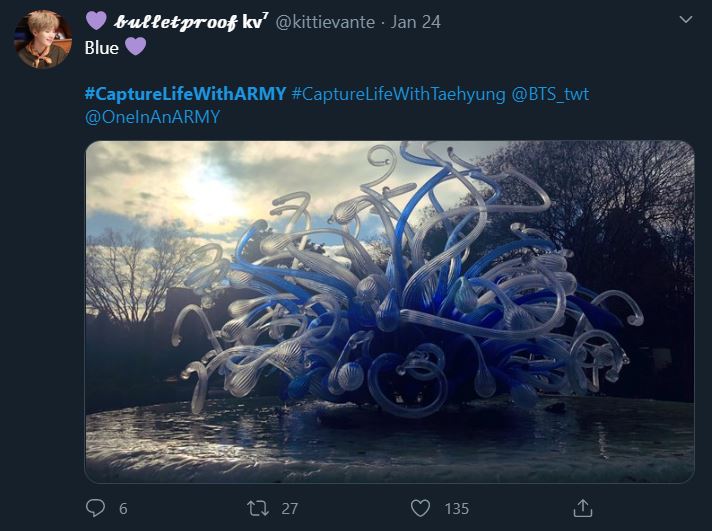 Tweet from an ARMY participating in the Bonus Mission Capture Life With ARMY. The photo shows an abstract glass sculpture positioned in the center of a frozen pond. The sculpture is made of frosted glass tubes that are white, light blue, and royal blue in colour. At the end of the tubes are glass bulbs that appear to have been made by blowing the glass.