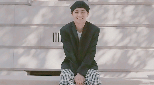 Gif of Taehyung smiling and dipping his head forward in laughter. Taehyung wears a black suit jacket, white and black checkered pants, and a black beret.