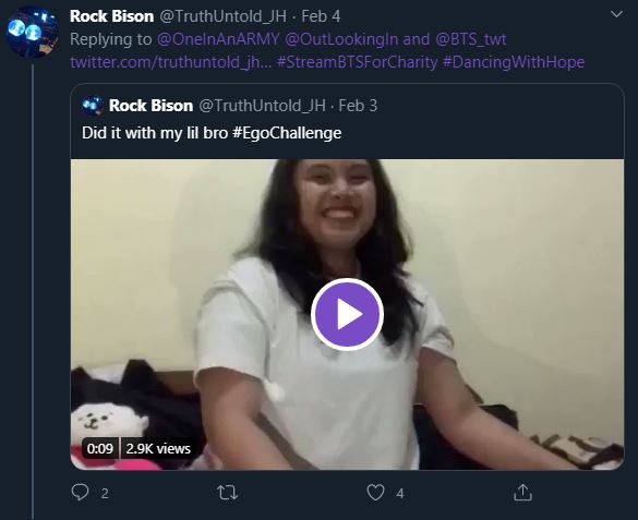 Screenshot of a tweet that says an ARMY did the Ego Challenge with their little brother. The still frame of the video shows the ARMY wearing a white t-shirt with chest length brown hair, smiling at the camera.