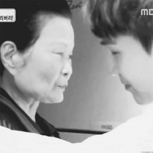 Greyscale gif showing Yoongi hugging an elderly Korean woman. Yoongi has short hair and has three earrings in his left ear, two in the shape of stars and one in the shape of a triangle.